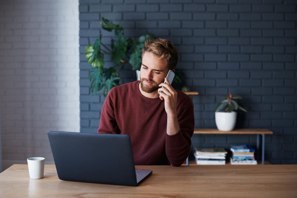 Meneer werkend achter laptop met telefoon aan zijn oor